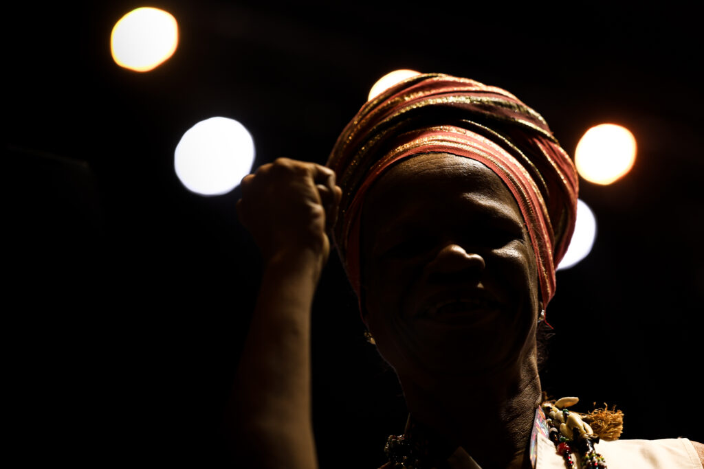 Mulher negra usando um turbante, com uma das mãos em punho, representando força para ilustrar o tema da igualdade racial no relatório Inesc 2025.