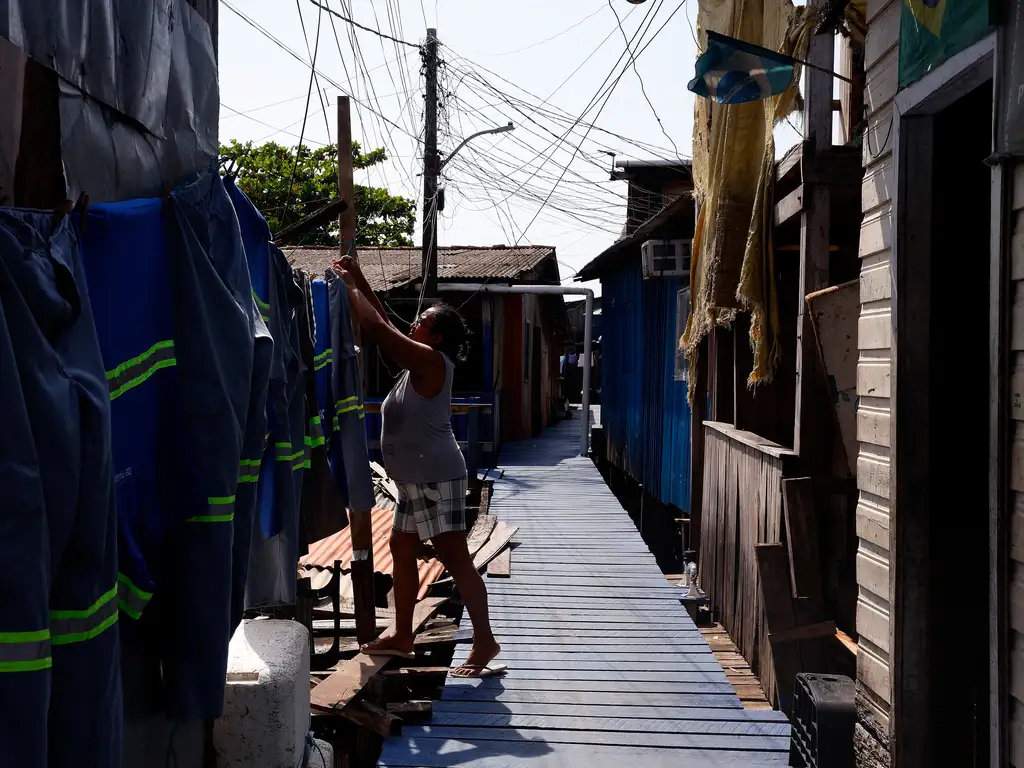 Mulher, em um corredor de madeira, entre palafitas, estendendo roupas, como ilustração sobre justiça climática