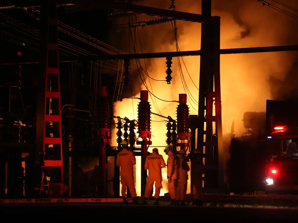 Incêndio em uma estação de energia e alguns trabalhadores tentando controlar o fogo. Imagem ilustra texto sobre transição energética, contas de luz e risco de apagão